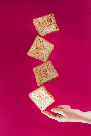 partial view of woman holding levitating toasts on finger isolated on pinkの写真素材