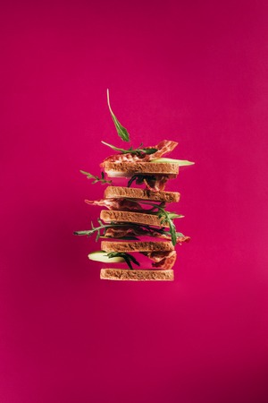 close up view of levitating sandwiches with bacon pieces and arugula isolated on pinkの写真素材