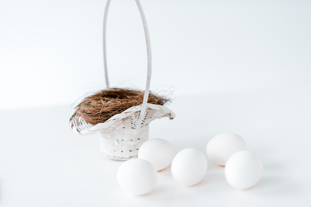 close-up view of white chicken eggs and nest in wicker basket on whiteの写真素材