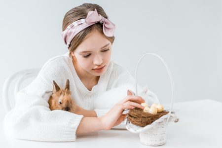 little girl hugging rabbit and looking at basket with easter eggs in nestの写真素材