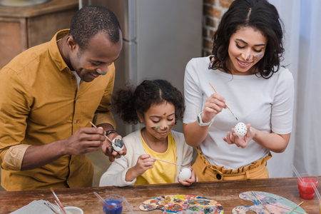 african american parents and daughter painting easter eggsの写真素材