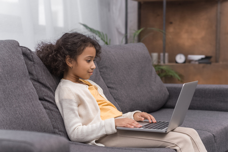 african american kid using laptop on sofa at homeの写真素材
