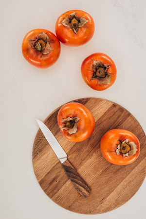 top view of persimmons with knife and wooden board isolated on whiteの写真素材