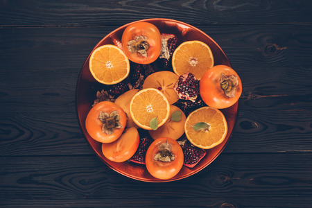 top view of persimmons with cut oranges and pomegranates on plate on tableの写真素材