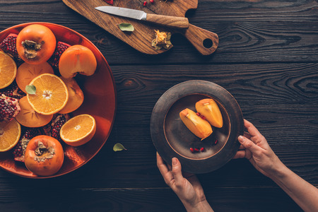 cropped image of woman holding plate with persimmon piecesの写真素材