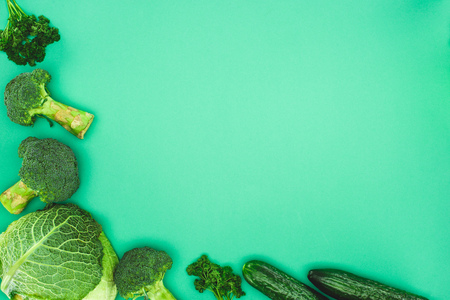 top view of fresh raw broccoli, parsley, cucumbers and savoy cabbage isolated on green backgroundの写真素材