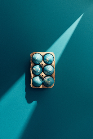 top view of blue easter eggs in tray, on blue with sunbeam