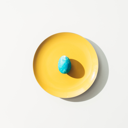 top view of shabby blue easter egg on yellow plate, on whiteの写真素材