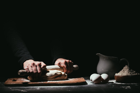cropped shot of person preparing dough with rolling pin on blackの写真素材