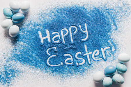 top view of happy easter sign made of blue sand with painted eggsの写真素材