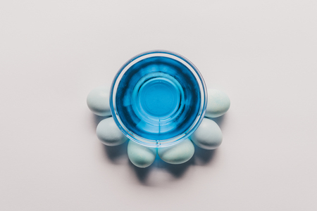 top view of glass with blue paint and chicken eggs on white surfaceの写真素材