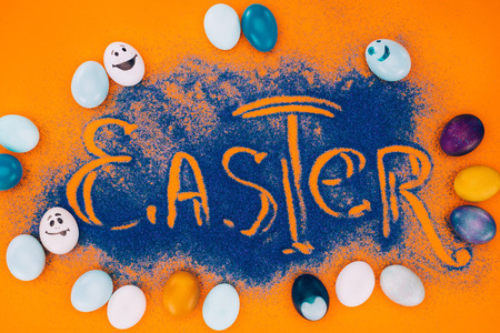 top view of easter sign made of blue sand with painted eggs orangeの写真素材