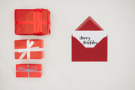 top view of red envelope with HAPPY BIRTHDAY lettering on paper and row of gift boxesの写真素材