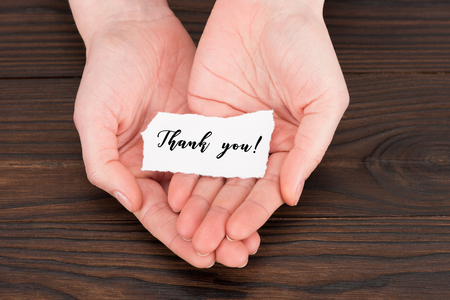 cropped shot of woman holding paper with thank you lettering over wooden tableの写真素材
