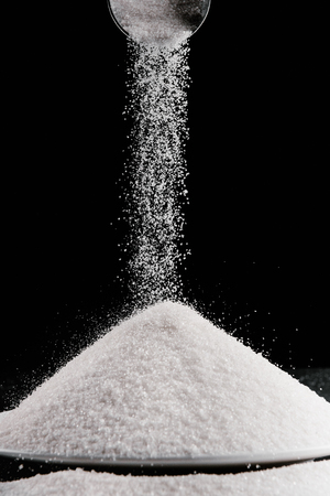 sugar falling from metal scoop on pile on plateの写真素材