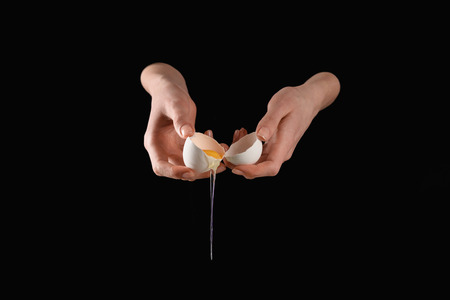 cropped image of woman holding broken dripping chicken egg isolated on blackの写真素材