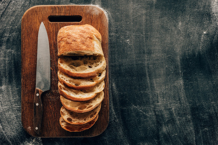 arranged pieces of ciabatta on cutting board with knife on dark surface with flour