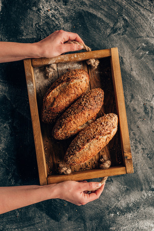 cropped shot of woman holding wooden box with loafs of bread in handsの写真素材