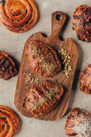 Flat lay with freshly baked sweet croissants with pistachio nuts on wooden cutting board on light surfaceの写真素材