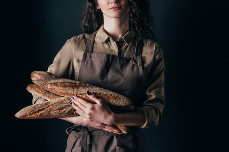 cropped shot of woman in apron holding french baguettes in hands isolated on blackの写真素材