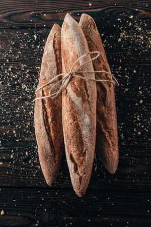 top view of french baguettes with rope on dark surface with flourの写真素材