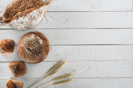 top view of healthy homemade loaves of bread and spikelets on wooden table