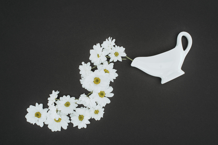 top view of white teapot with daisy flowers over black backgroundの写真素材