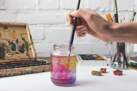 cropped shot of artist putting paint brush into glass jar with water at workplaceの写真素材