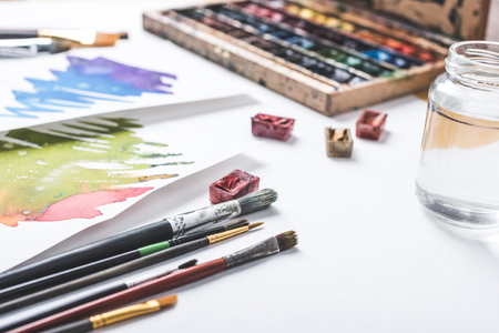 close-up view of paints, paintbrushes and watercolor sketches at designer workplace の写真素材