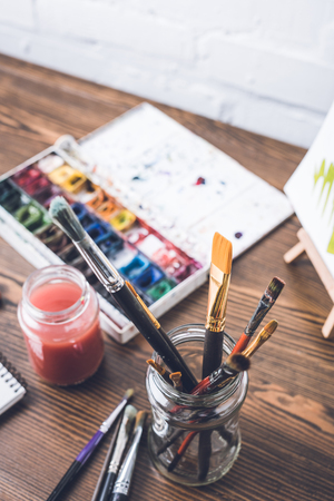 selective focus of watercolor paints and paintbrushes at designer workplaceの写真素材