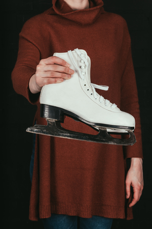 cropped image of woman in holding pair of white skates isolated on blackの写真素材