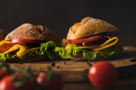 sandwiches with cheese on wooden board on table with cherry tomatoes on foregroundの写真素材