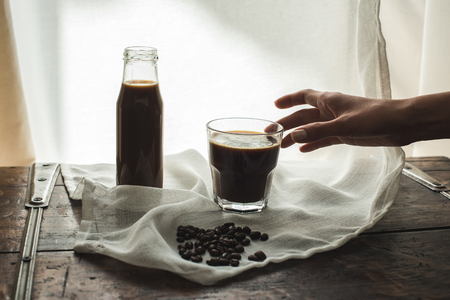 Person taking glass of coffee from cloth with roasted coffee beansの写真素材