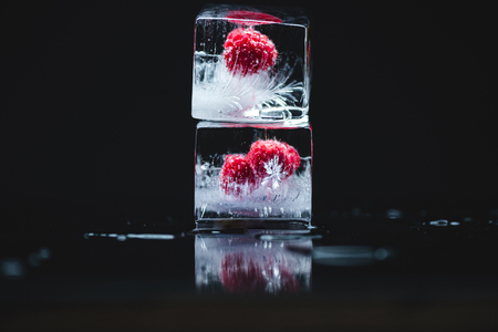 close-up view of ripe juicy raspberries frozen in ice cubes on black の写真素材