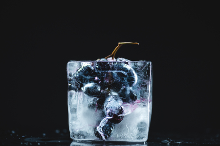 close-up view of frozen ripe sweet grape in ice cube on blackの写真素材