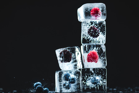 ripe juicy seasonal berries frozen in ice cubes stacked on blackの写真素材