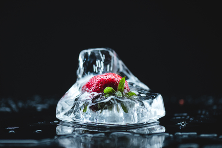 close-up view of red strawberry in melting ice cube on blackの写真素材
