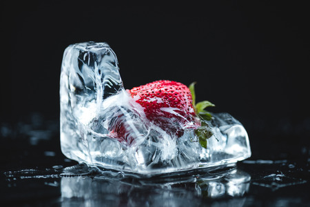 close-up view of ripe strawberry in melting ice cube on blackの写真素材