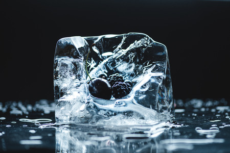 ripe cherry and blackberries in transparent melting ice cube on blackの写真素材