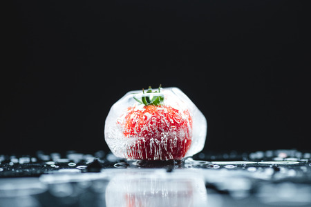 close-up view of ripe cherry tomato frozen in ice cube on black の写真素材