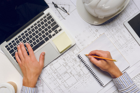 cropped shot of architect working on laptop and making notes in notebookの写真素材