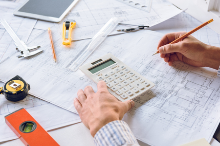 cropped shot of architect working with blueprints and calculator at workplaceの写真素材