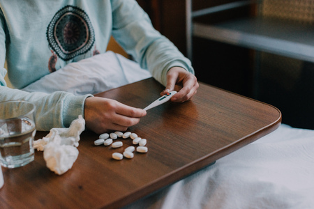cropped shot of sick person holding thermometer above table with pills の写真素材