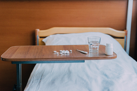 pills, glass of water and thermometer on table in hospitalの写真素材