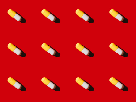 close-up view of pattern made from white and yellow medical capsules on redの写真素材