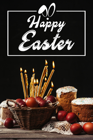 happy easter inscription in frame, burning candles, easter cakes and painted eggs on black