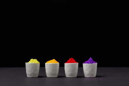 row of colorful holi paint in four bowls on black, Hindu spring festival
