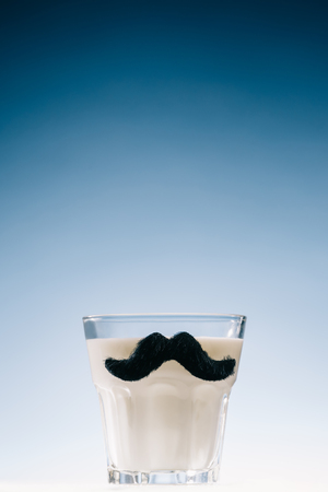 Transparent glass with mustaches filled with milk isolated on blue backgroundの写真素材