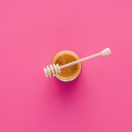 top view of honey with wooden honey stick isolated on pinkの写真素材