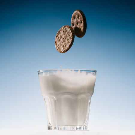 Two biscuits falling into glass of milk isolated on blue background